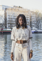 L'image représente une jeune fille dans l'espace public, regardant frontalement l'appareil photo. 