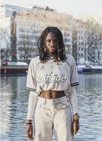 L'image représente une jeune fille dans l'espace public, regardant frontalement l'appareil photo. 